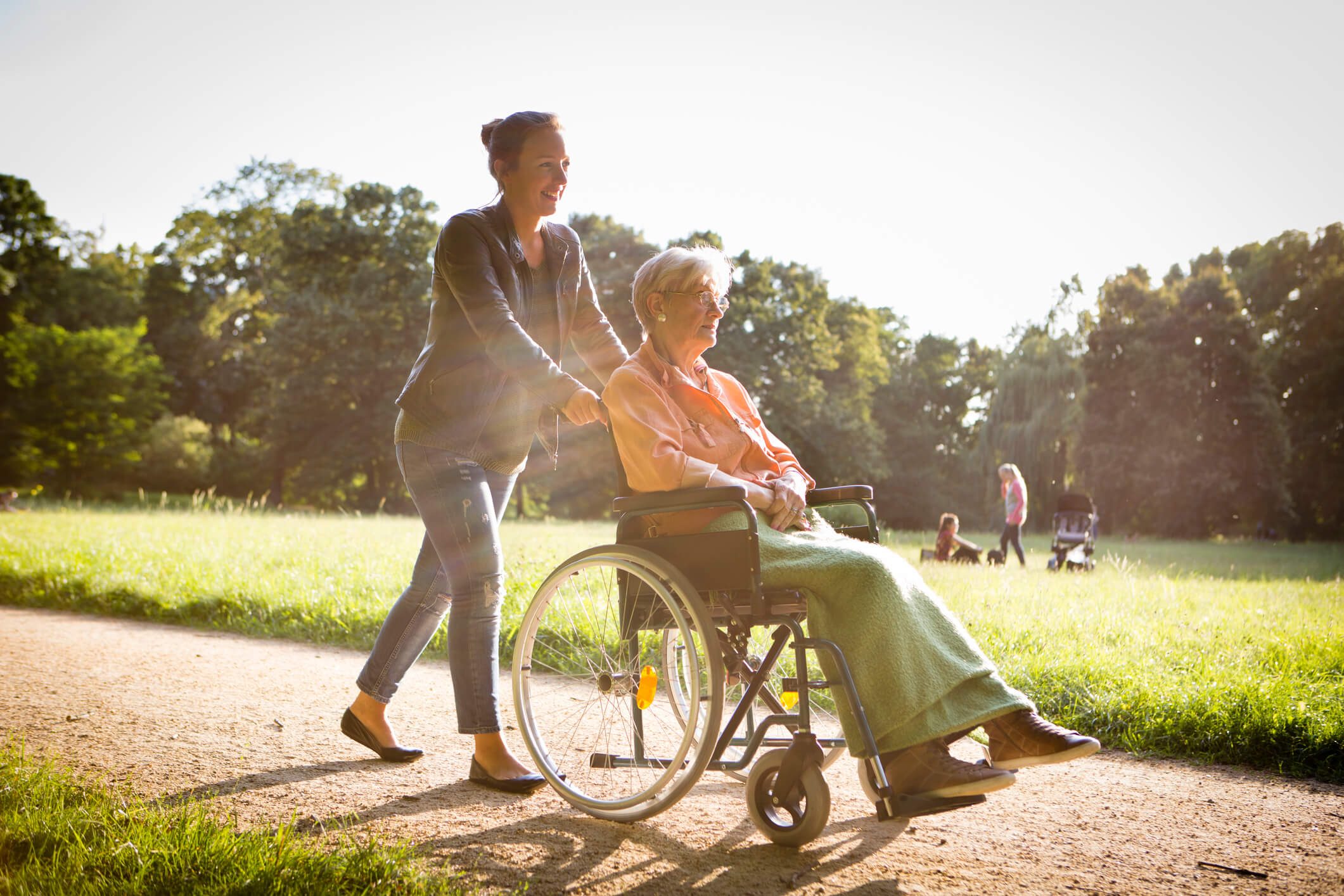 Junge Frau senior Frau im Rollstuhl Schieben durch einen park